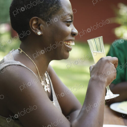 A woman sitting at a table outdoors in a garden, taking a drink. A woman sitting at a table outdoors in a garden, taking a drink.