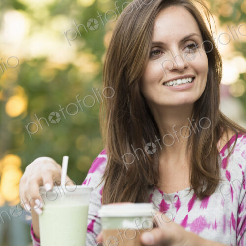 A woman sitting at a table outdoors, with a smoothie on the table. A woman sitting at a table outdoors, with a smoothie on the table.