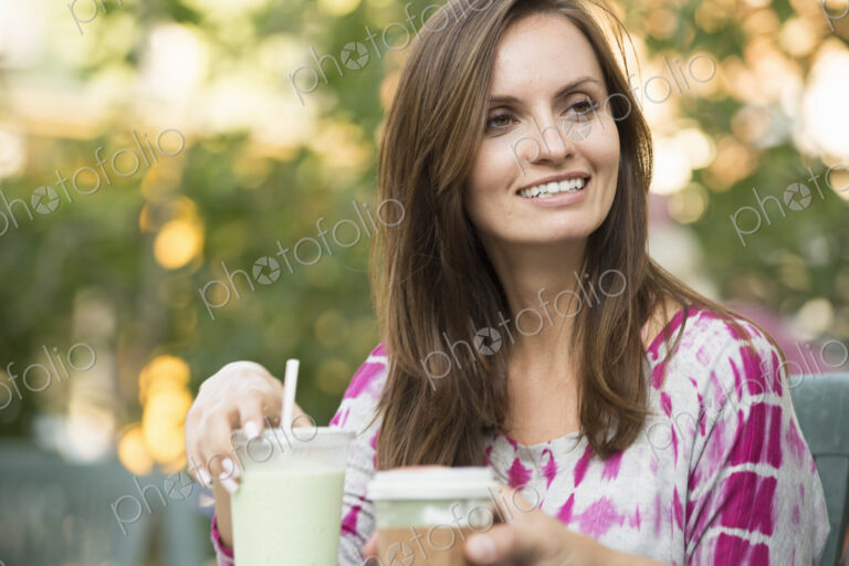 A woman sitting at a table outdoors, with a smoothie on the table.
