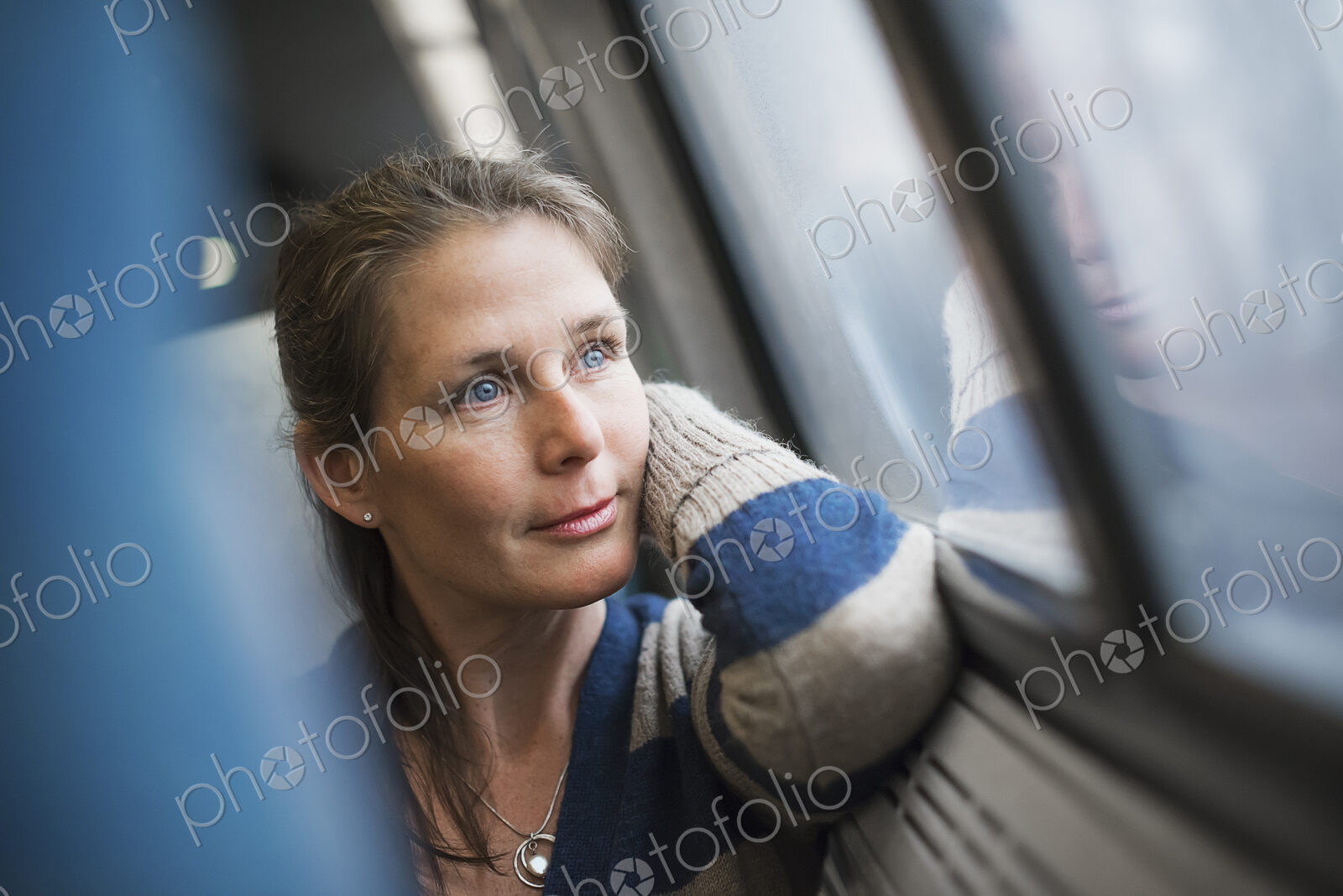 A woman sitting at a window seat in a train carriage, resting her head on her hand.…