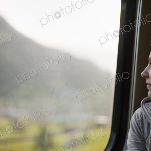 A woman sitting by a train window looking out at the landscape.