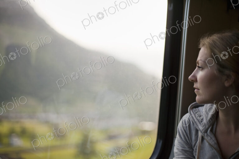 A woman sitting by a train window looking out at the landscape.