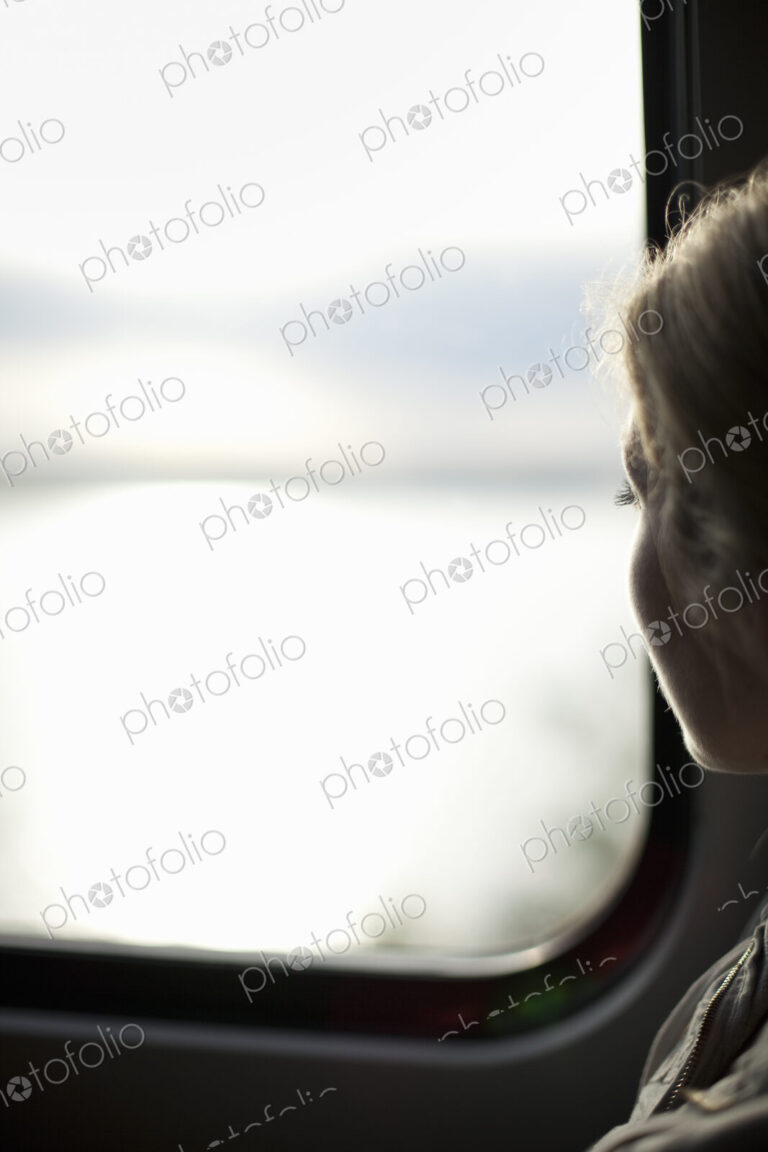 A woman sitting by a train window looking out at the view.