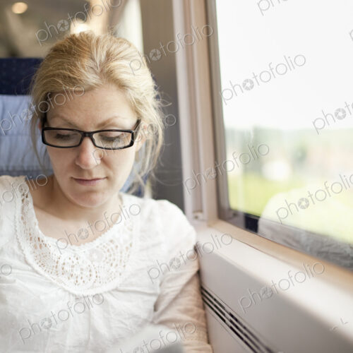 A woman sitting by a train window, reading a book.