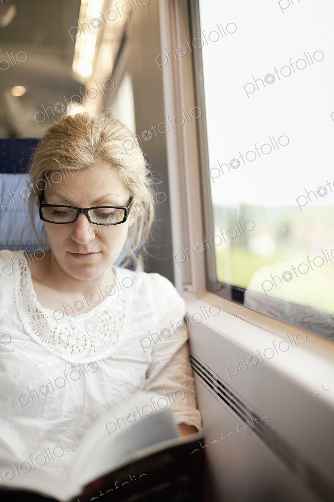 A woman sitting by a train window, reading a book.