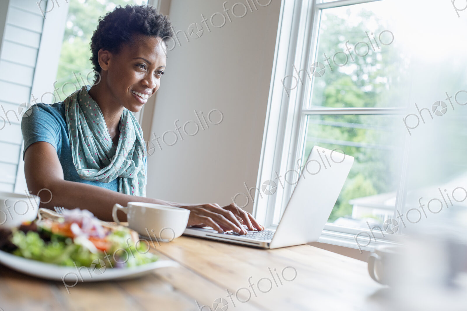 A woman sitting in a cafe with a cup of coffee and a meal. Using a laptop.