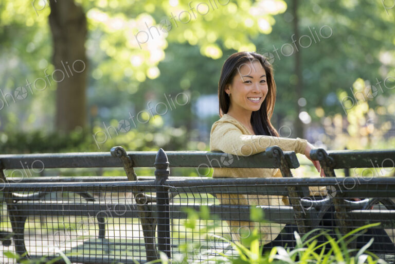 A woman sitting in a city park on a bench in the sunshine.