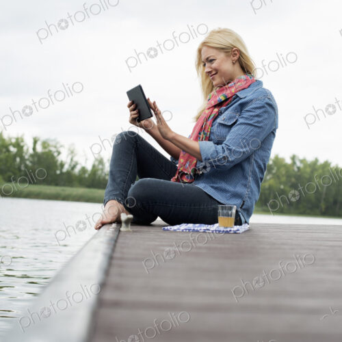 A woman sitting on a jetty by a lake, using a digital tablet. A woman sitting on a jetty by a lake, using a digital tablet.