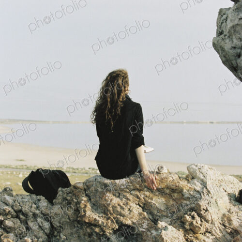 A woman sitting on a rock looking out over water.