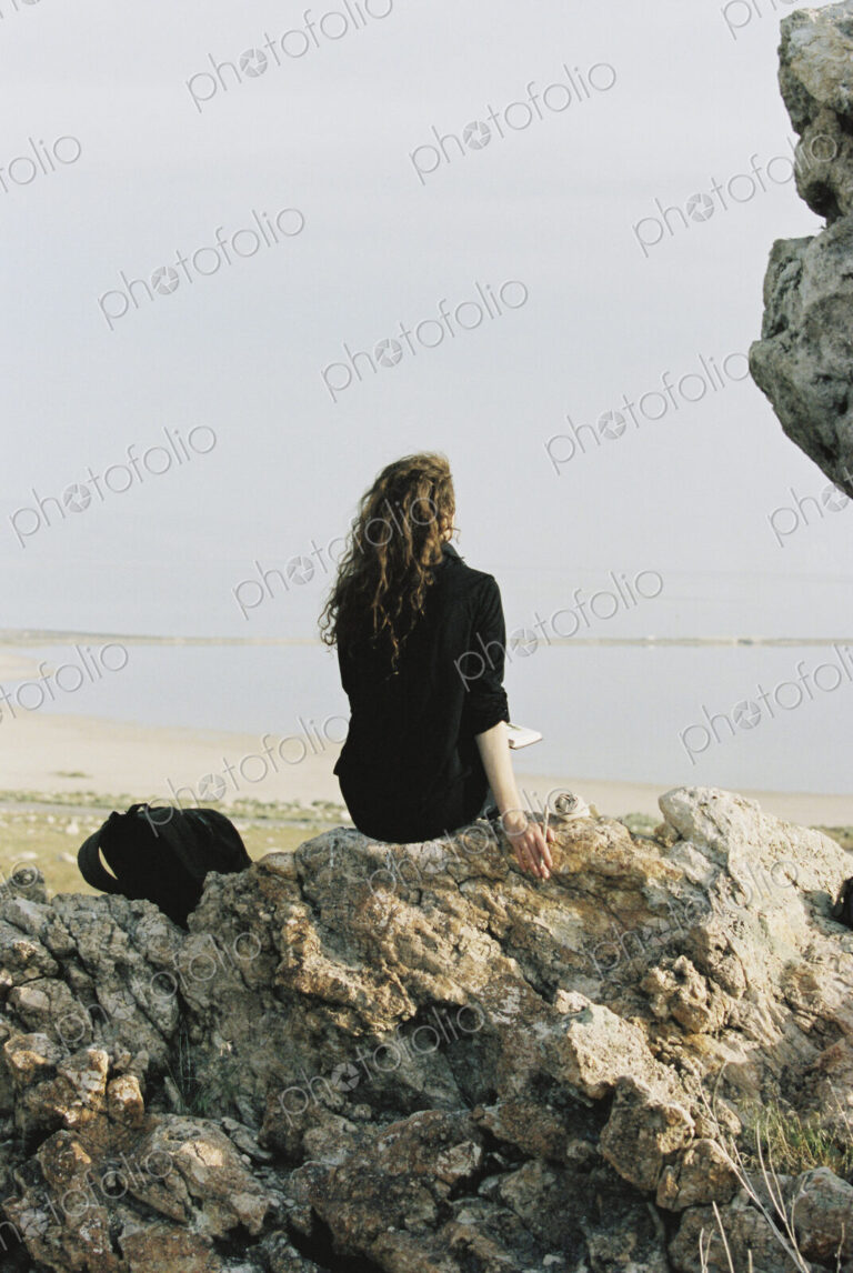 A woman sitting on a rock looking out over water.