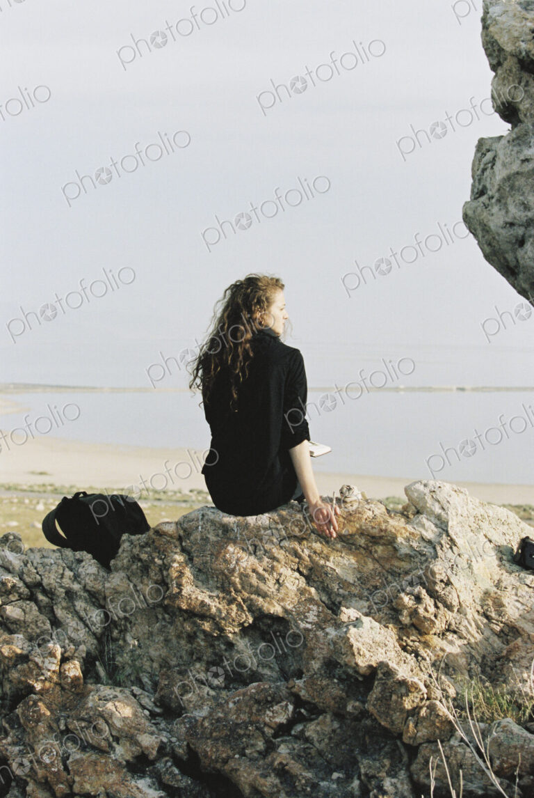 A woman sitting on a rock looking out over water.
