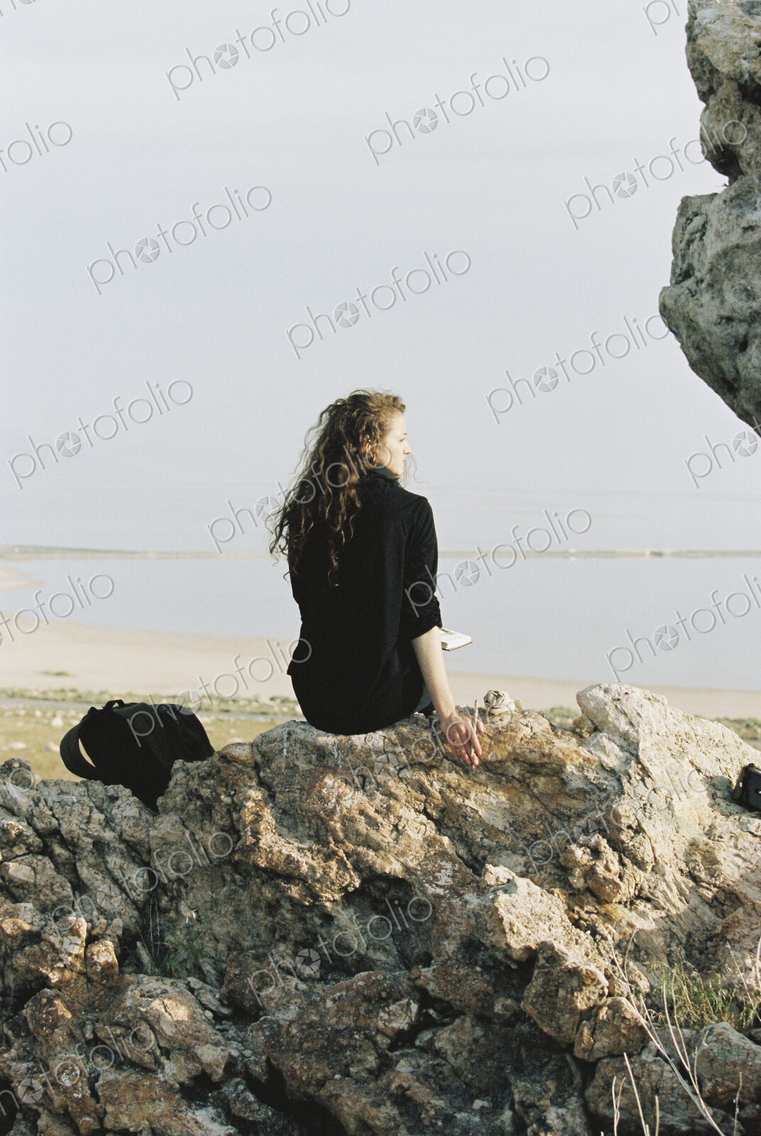 A woman sitting on a rock looking out over water.
