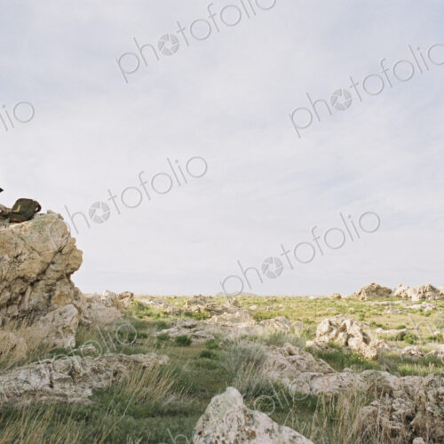 A woman sitting on a rock, writing in a notebook, a backpack lying by her feet. A woman sitting on a rock, writing in a notebook, a backpack lying by her feet.
