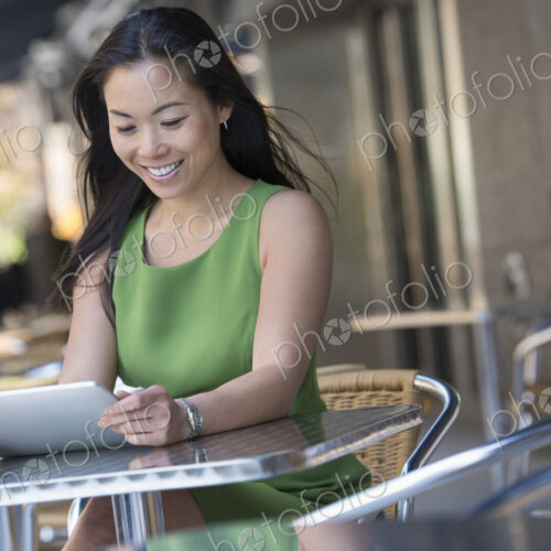 A woman sitting outdoors at a cafe table using a digital tablet. A woman sitting outdoors at a cafe table using a digital tablet.