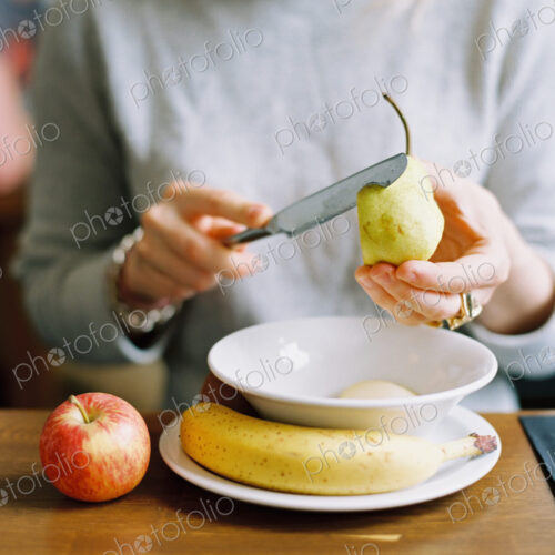 A woman slicing a fresh pear. Apple and banana.
