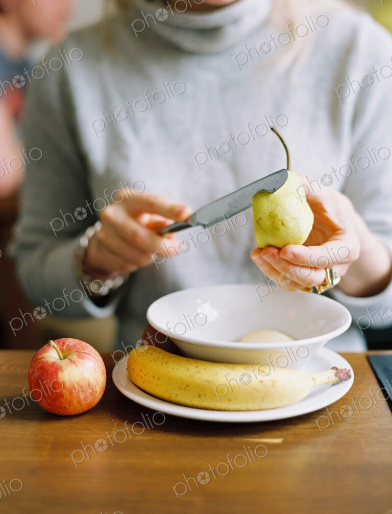 A woman slicing a fresh pear. Apple and banana.