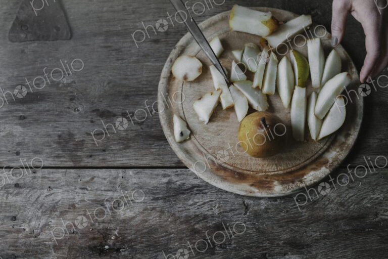 A woman slicing fresh fruit, pears on a chopping board.