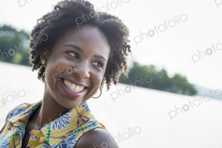 A woman smiling and laughing on a lake shore.