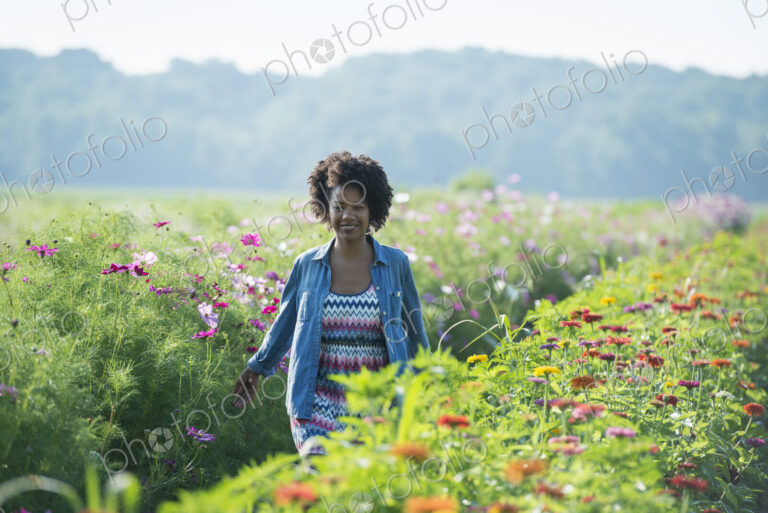 A woman standing among the flowers growing in the fields. Pink and white cosmos blooms.