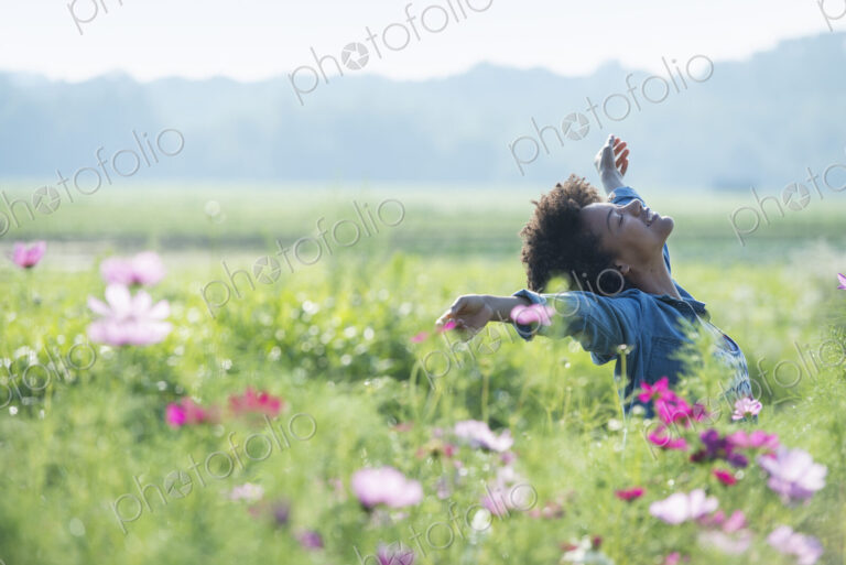 A woman standing among the flowers with her arms outstretched. Pink and white cosmos…