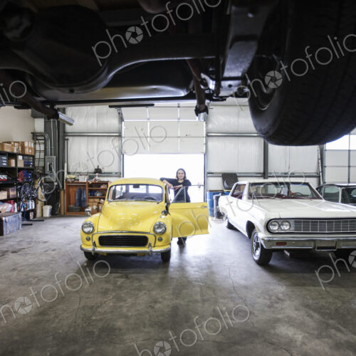 A woman standing by the open door of a bright yellow Morris Minor car, an English… A woman standing by the open door of a bright yellow Morris Minor car, an English…