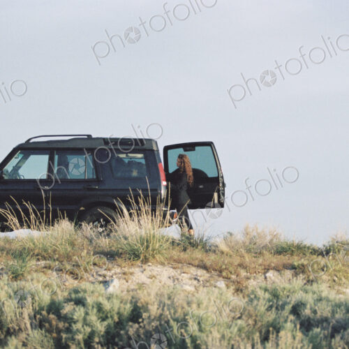 A woman standing by the open rear door of a 4x4 in open space.