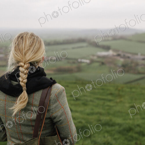 A woman standing in a hilltop looking at the view.