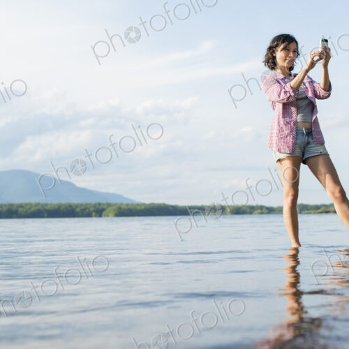 A woman standing in a lake in summer. Taking a photograph.