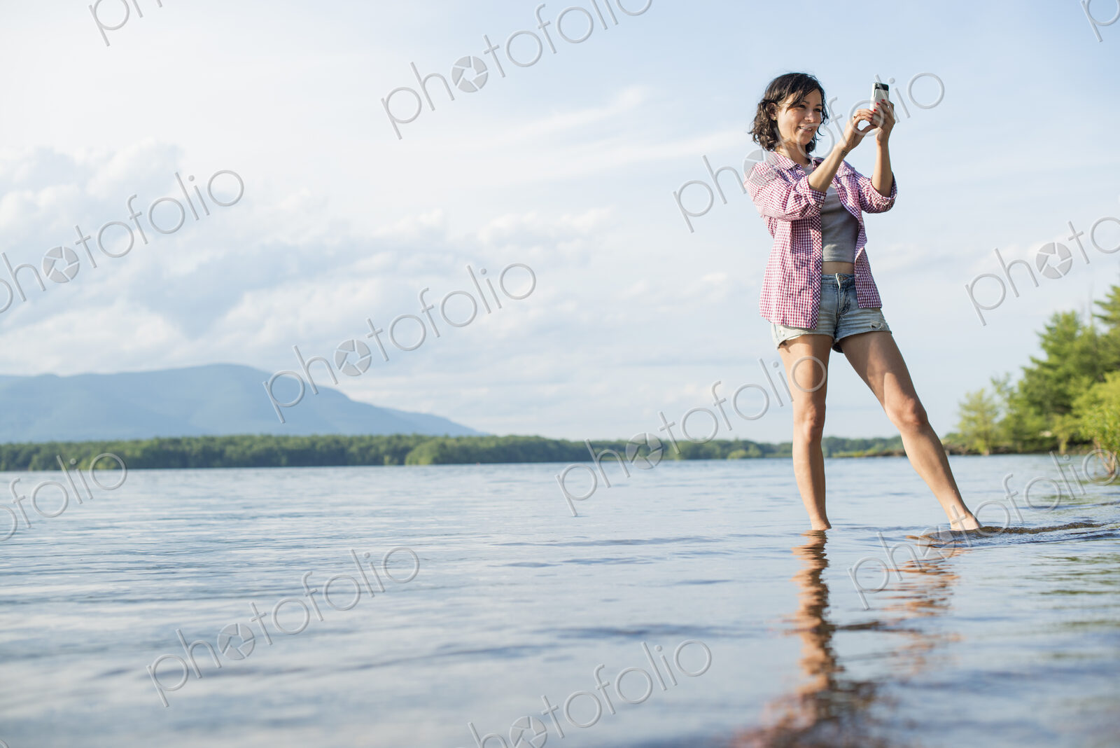 A woman standing in a lake in summer. Taking a photograph.