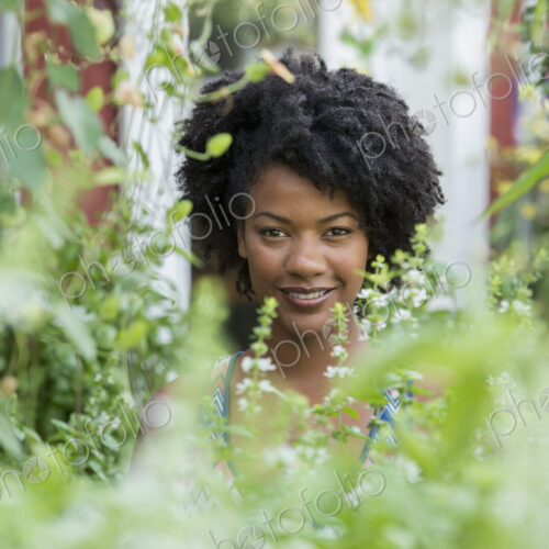 A woman standing in a plant nursery, surrounded by plants, flowers and foliage. A woman standing in a plant nursery, surrounded by plants, flowers and foliage.