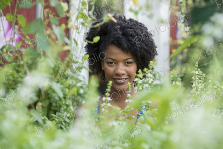 A woman standing in a plant nursery, surrounded by plants, flowers and foliage.