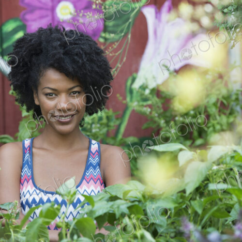 A woman standing in a plant nursery, surrounded by plants, flowers and foliage. A woman standing in a plant nursery, surrounded by plants, flowers and foliage.