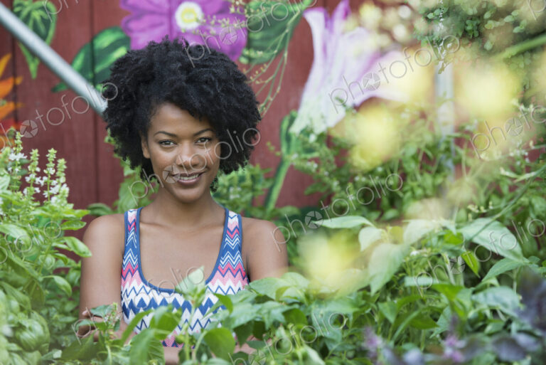 A woman standing in a plant nursery, surrounded by plants, flowers and foliage.