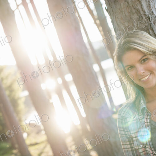 A woman standing in the shadows of tall trees on the shores of a lake in summer. A woman standing in the shadows of tall trees on the shores of a lake in summer.