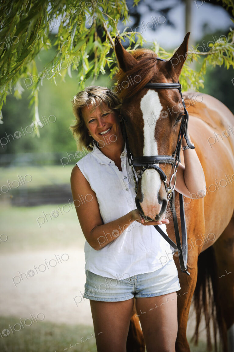 A woman standing next to a bayhorse with a halter rein.