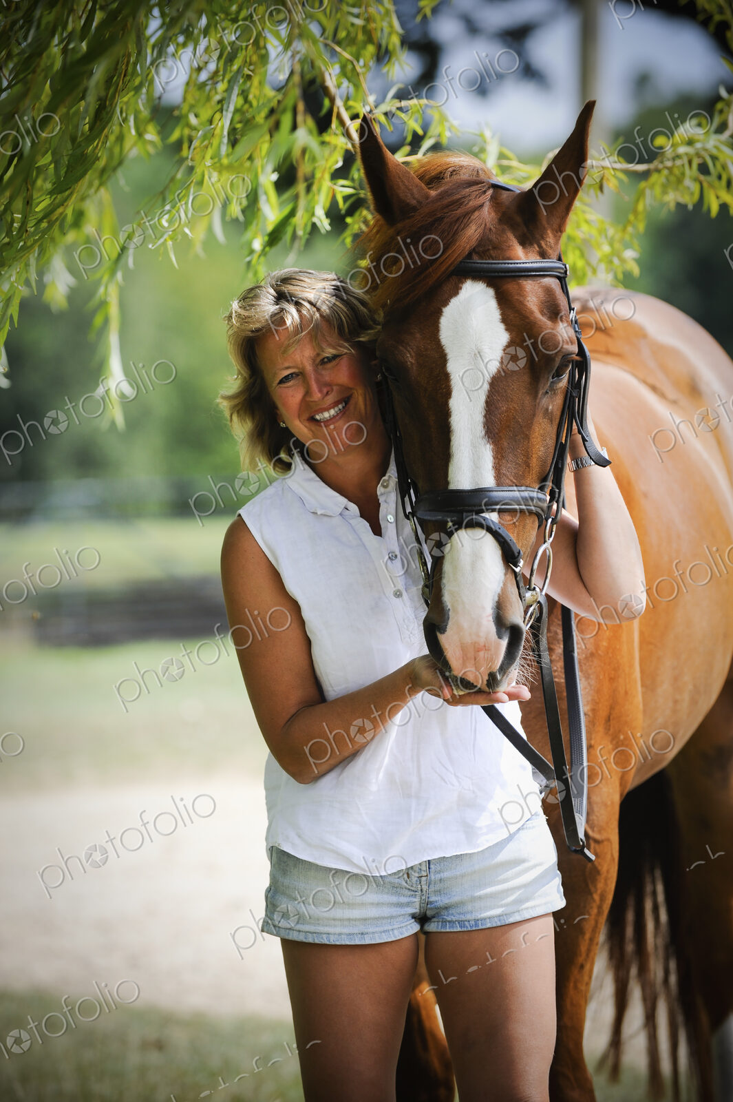 A woman standing next to a bayhorse with a halter rein.