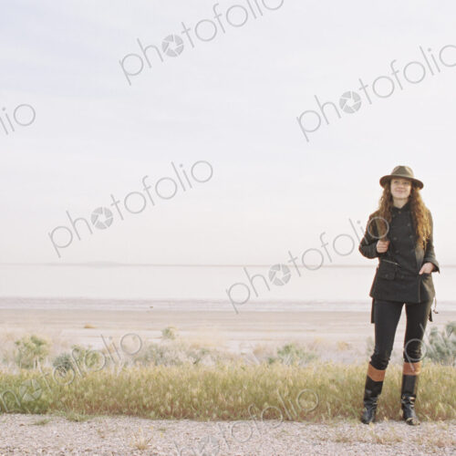 A woman standing on a country road, wearing a hat and carrying a backpack.
