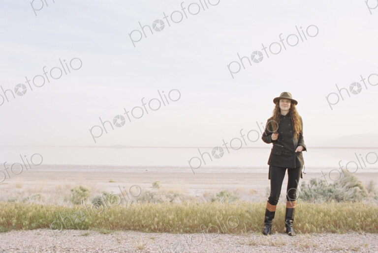 A woman standing on a country road, wearing a hat and carrying a backpack.