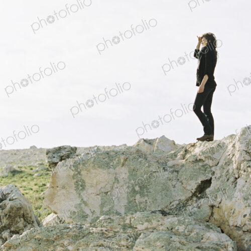 A woman standing on a rock shielding her eyes from the sun with her hand.