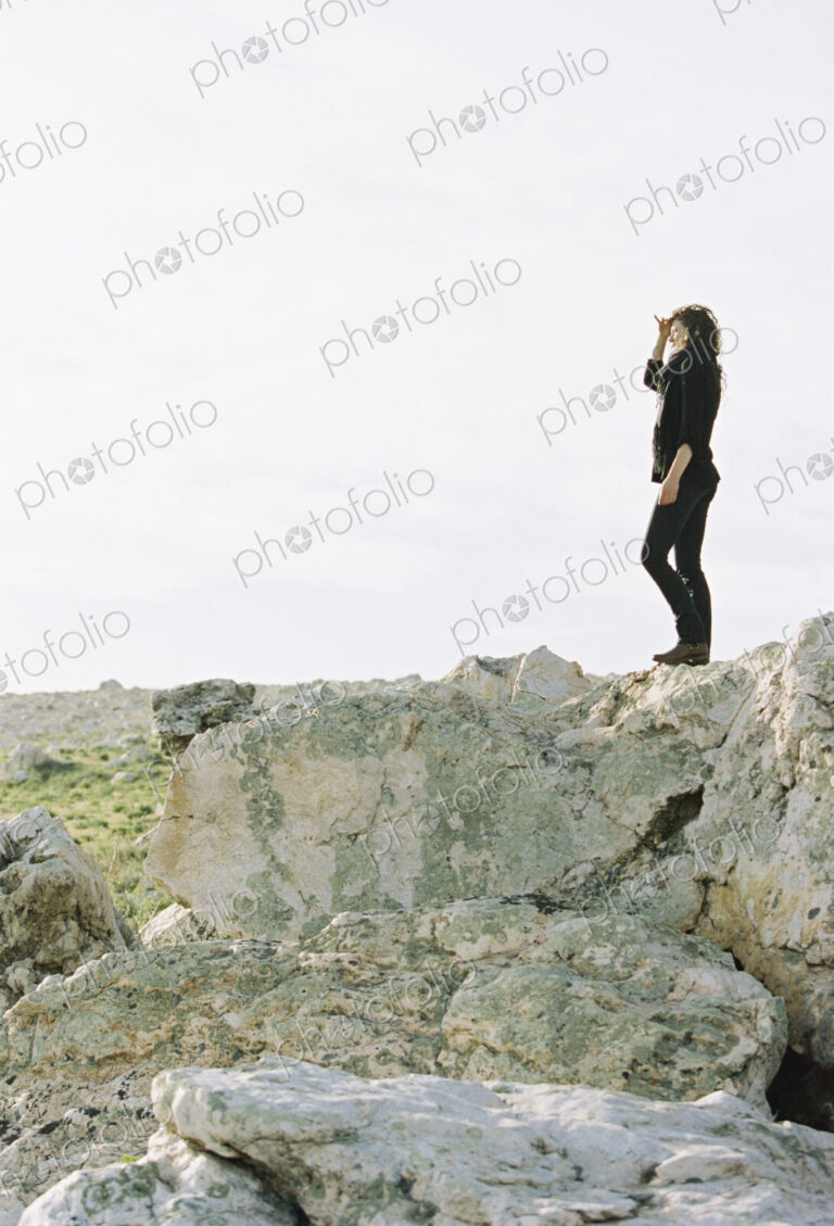 A woman standing on a rock shielding her eyes from the sun with her hand.