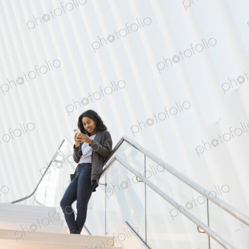 A woman standing on a stairway in a large atrium checking her phone. A woman standing on a stairway in a large atrium checking her phone.