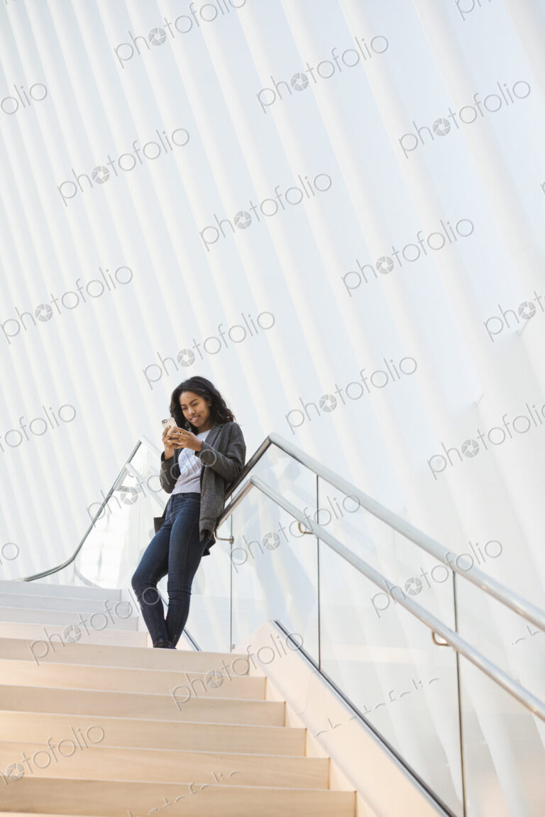 A woman standing on a stairway in a large atrium checking her phone.