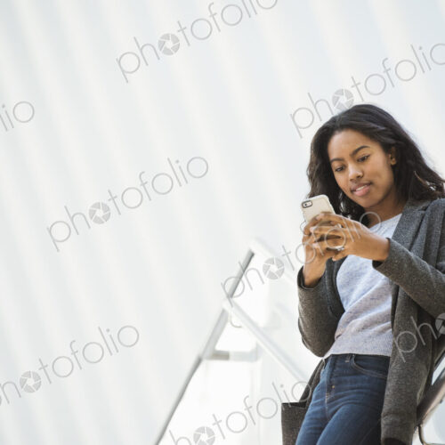 A woman standing on a stairway in an open space, texting on her phone. A woman standing on a stairway in an open space, texting on her phone.
