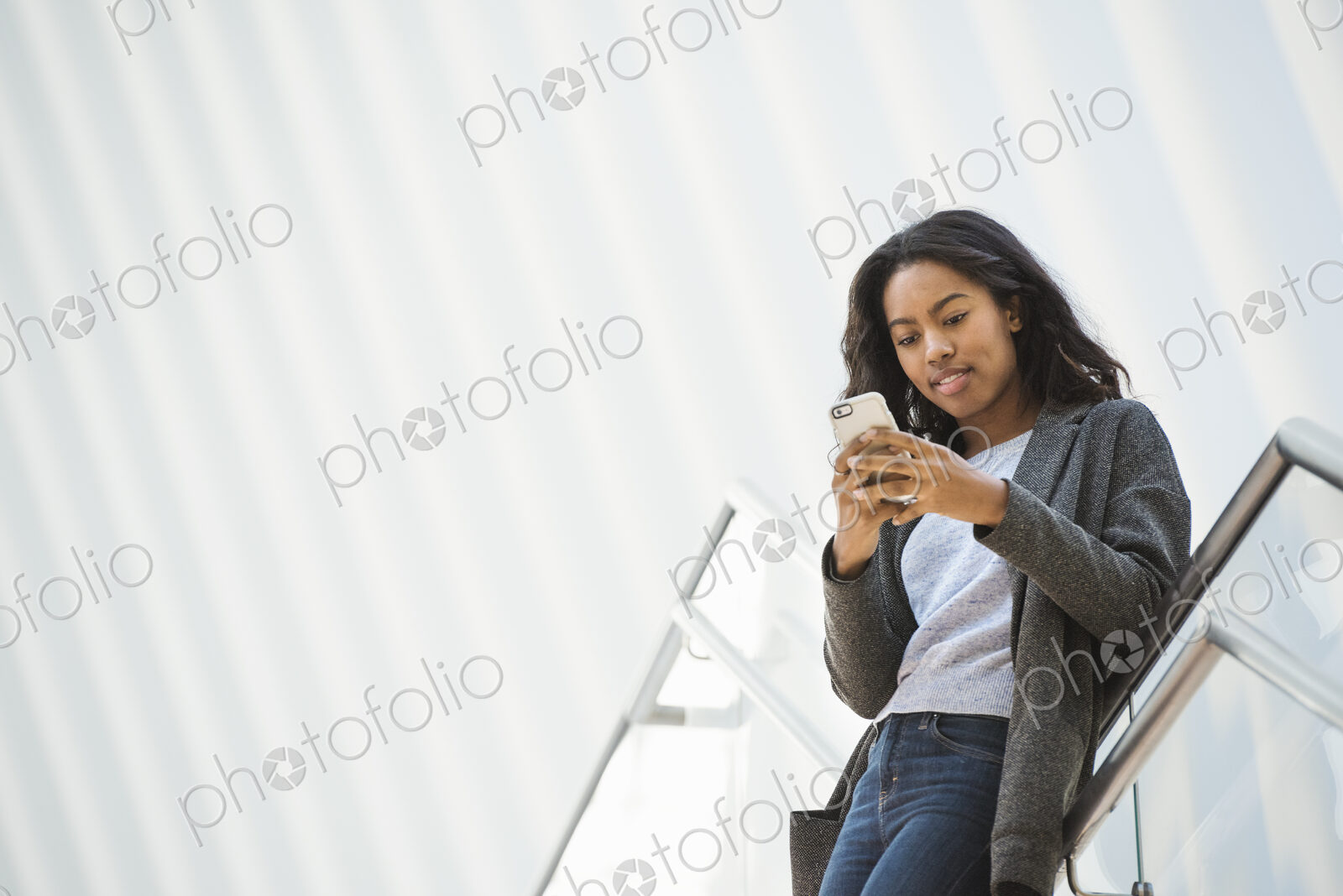 A woman standing on a stairway in an open space, texting on her phone.