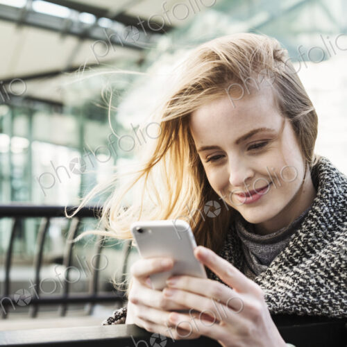 A woman standing outdoors in the city, checking her smart phone. A woman standing outdoors in the city, checking her smart phone.