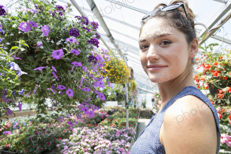 A woman standing surrounded by flowering plants in a commercial greenhouse.