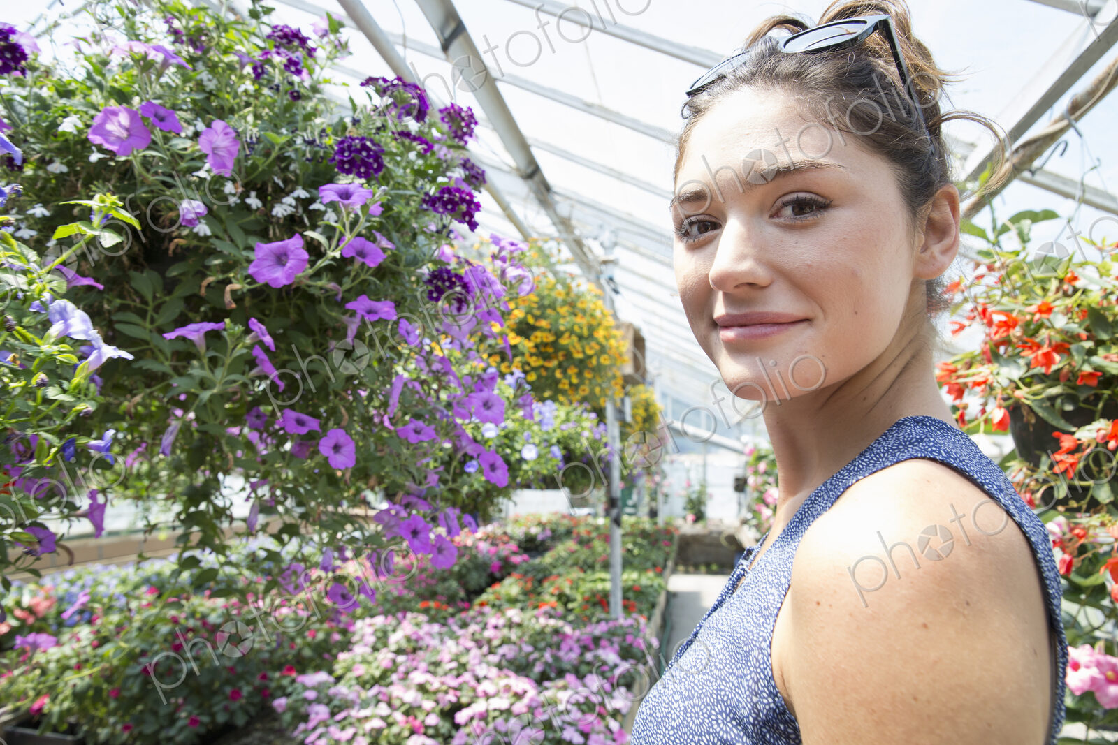 A woman standing surrounded by flowering plants in a commercial greenhouse.