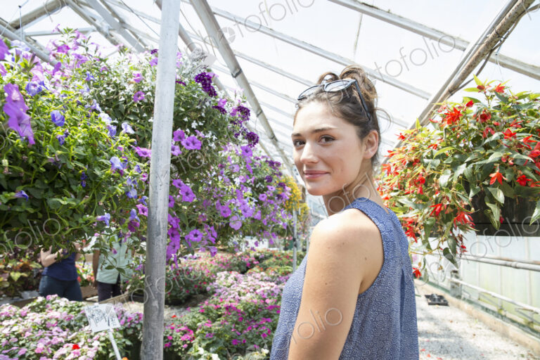 A woman standing surrounded by flowering plants in a commercial greenhouse.