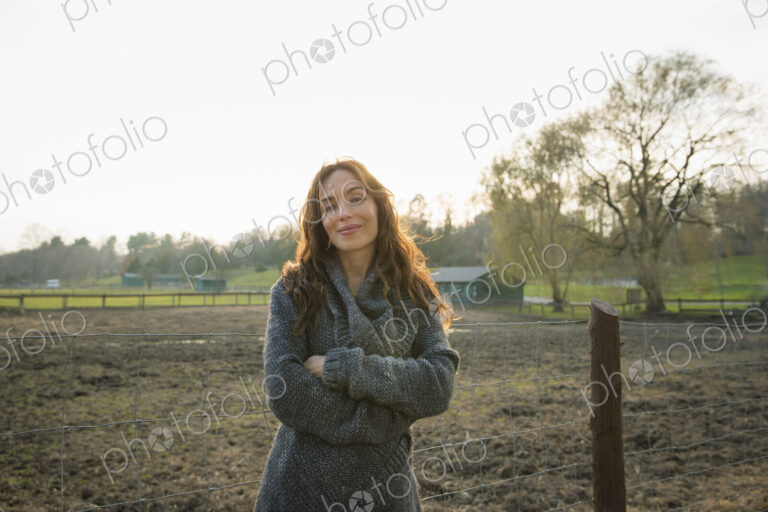 A woman standing with arms folded, by a paddock in an animal sanctuary.