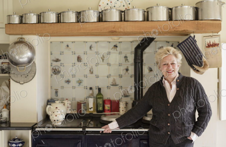 A woman standing with her back to a range cooker, in her kitchen.